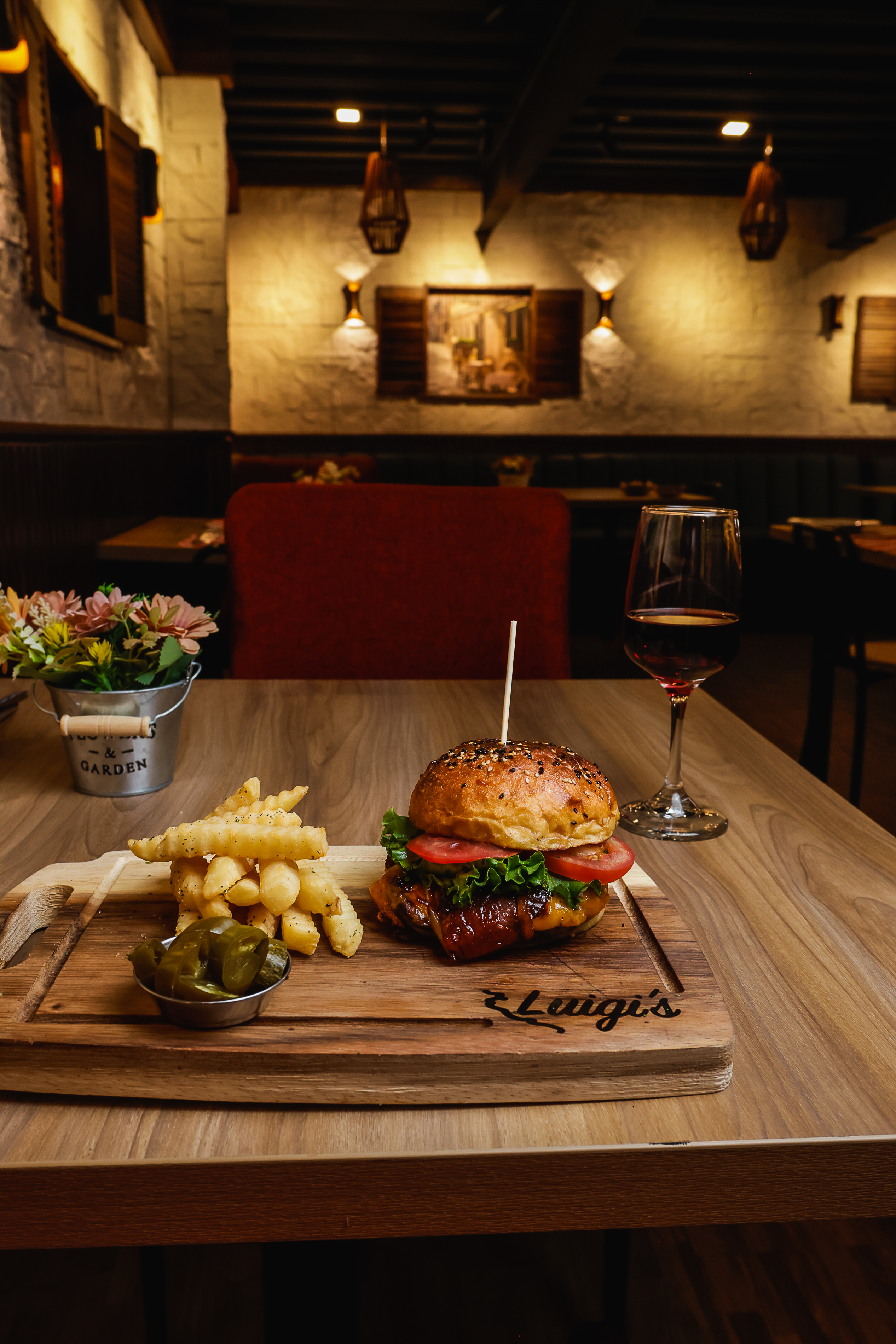 Hamburguesa de la casa con papas a la francesa y copa de vino sobre tabla de madera Luigi's
